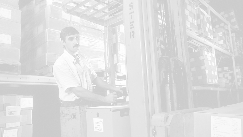 a photograph of a man operating a standing forklift in a warehouse.