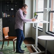 a photo of a person working at a standing desk in front of a large window looking over the city of Vancouver.